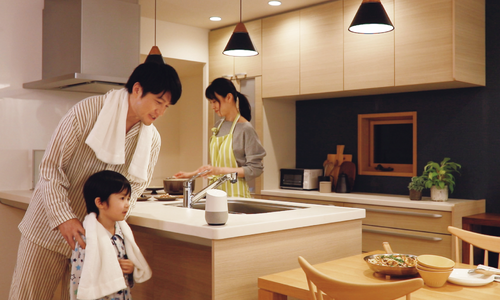 キッチンで料理をする母とお風呂上がりの父と子の写真