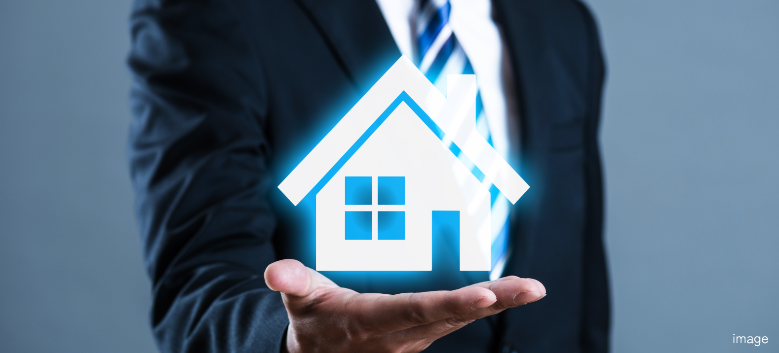 家のアイコンを手のひらに示すスーツ姿の人物の写真